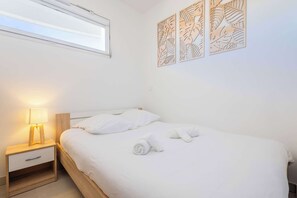 En pænt redt seng med hvide sengetøj, en sengetavlelampe og et billede på væggen.