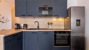 Una cocina moderna con armarios oscuros, un refrigerador de acero inoxidable, un horno empotrado y una encimera de madera.
