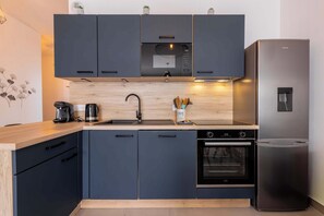 A modern kitchen with dark cabinets, a stainless steel refrigerator, a built-in oven, and a wooden countertop. - Valras'Loc Archipel Panarea Sea View and Comfort (Valras-Plage)