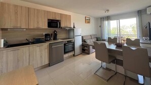 A modern kitchen with wooden cabinets, a microwave, a coffee maker, and a refrigerator. - Agde’Loc – The Sunny Cocoon (Vias)
