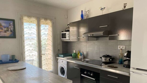 A modern kitchen with stainless steel appliances, a built-in washing machine, and a large window with a view. - Downtown Apartment – 100 m from the Beach (Vendres)