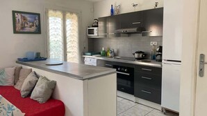 A compact kitchen with a built-in stove, microwave, and oven. There is a small dining area with a red table and cushions. - Downtown Apartment – 100 m from the Beach (Vendres)