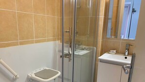A bathroom with a glass shower enclosure, a white sink, and a small white bench. - Downtown Apartment – 100 m from the Beach (Vendres)
