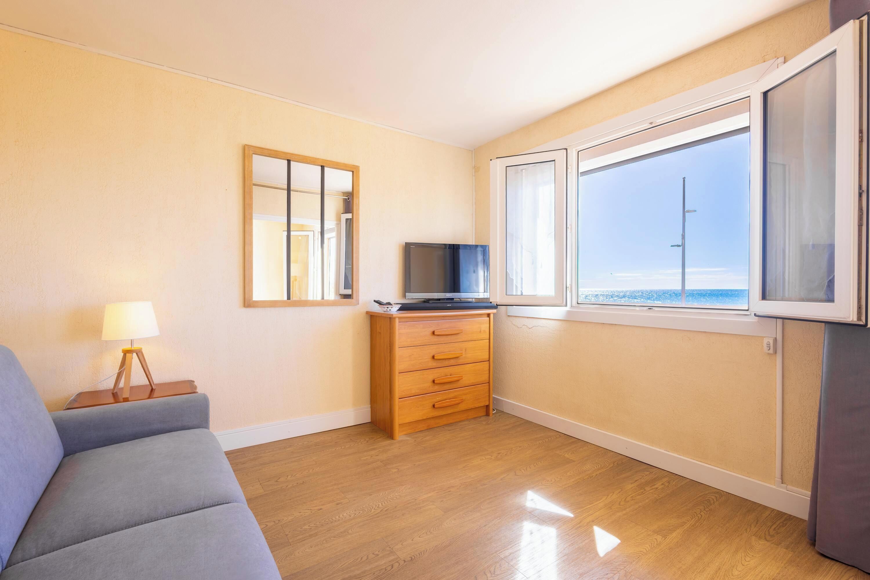 A room with a sofa, a wooden dresser, a television, and a window with a view.