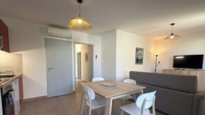 A modern living room with a dining area, a grey sofa, and a TV mounted on the wall. - T2 with Terrace & Pool 300m from the Beach (Sérignan)