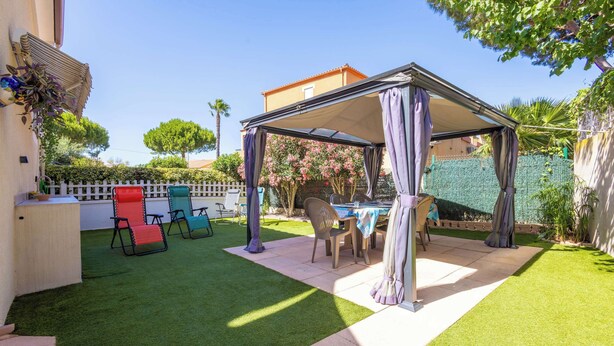 A covered patio area with a table and chairs, surrounded by artificial grass and a white fence. - Les Jardins Du Soleil – Comfortable Holiday Home (Valras-Plage)
