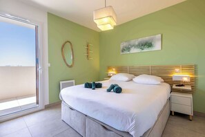 Quarto com cama, luminárias de cabeceira, mesa de cabeceira, janela e uma obra de arte na parede.