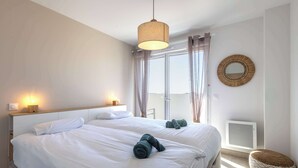 A hotel room with two beds, a large window with curtains, a round mirror, and a small ottoman. - Casa Naia - 4-Star Prestige Duplex Valras-Plage (Sérignan)