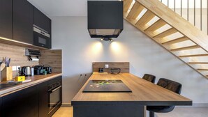 A modern kitchen with a central island, black cabinets, and a wooden staircase. - Casa Naia - 4-Star Prestige Duplex Valras-Plage (Sérignan)