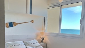 A bed with striped bedding, a wooden paddle, and a lamp on a bedside table. - Bel Horizon – Magnificent apartment with panoramic sea view (Valras-Plage)
