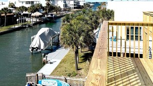 A waterfront property with a wooden deck, a covered dock, and a view of the water and buildings in the background. - Coastal Cottage (Navarre)