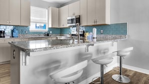 A modern kitchen with granite countertops, stainless steel appliances, and a central island with bar stools. - Coastal Cottage (Navarre)