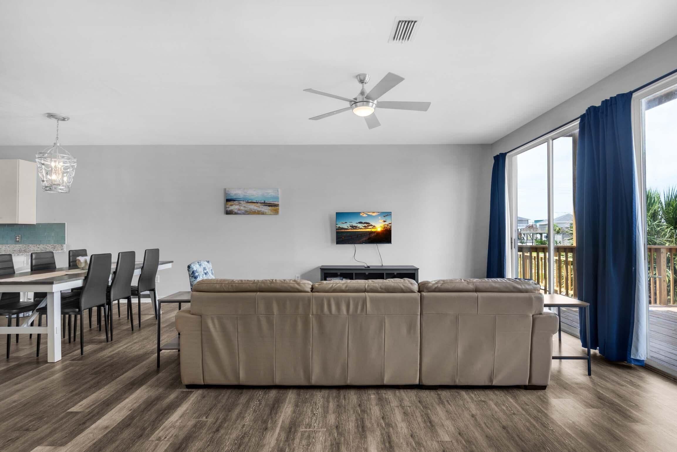 A modern living room with a sofa, dining table, chairs, and a ceiling fan.