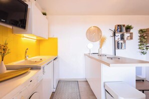 Een moderne keuken met een inbouwvaatwasser, een houten aanrecht, een hangklok en een boekenkast met boeken en planten.