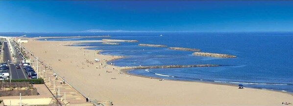 A coastal beach with a promenade, clear skies, and calm sea.