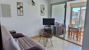 A living room with a sofa, a TV, and a balcony with a table and chairs.