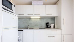 A compact kitchen with white cabinets, a microwave, a coffee maker, and a washing machine. - Valras Apartment with Sea View (Valras-Plage)