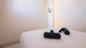 A hotel room with a bed, two rolled towels, and a door with a poster. - Valras Apartment with Sea View (Valras-Plage)