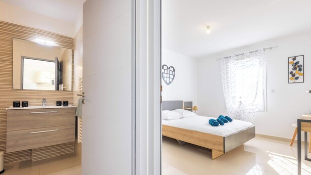 A modern bedroom with a wooden bed, a bedside table, a mirror, and a bathroom with a vanity and sink.