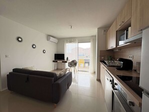 A modern apartment with a sofa, a TV, a kitchen with a microwave, and a balcony with chairs.