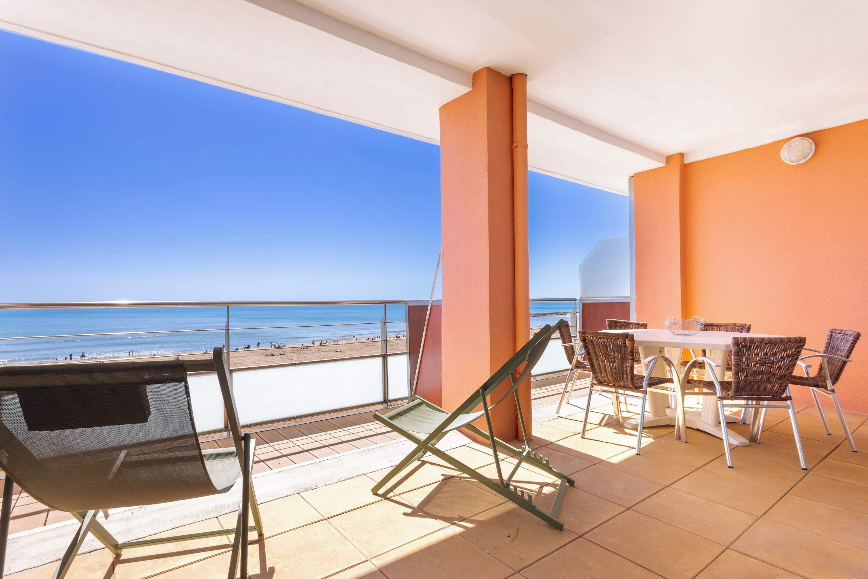 Ein Balkon mit Tisch und Stühlen mit Blick auf einen Strand.