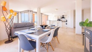 Une cuisine moderne avec des meubles blancs, un coin repas avec une table dressée pour quatre personnes et une grande fenêtre laissant entrer la lumière naturelle.