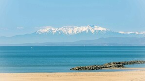 Un paysage côtier avec une plage de sable, une mer calme et, au loin, des montagnes aux sommets enneigés.