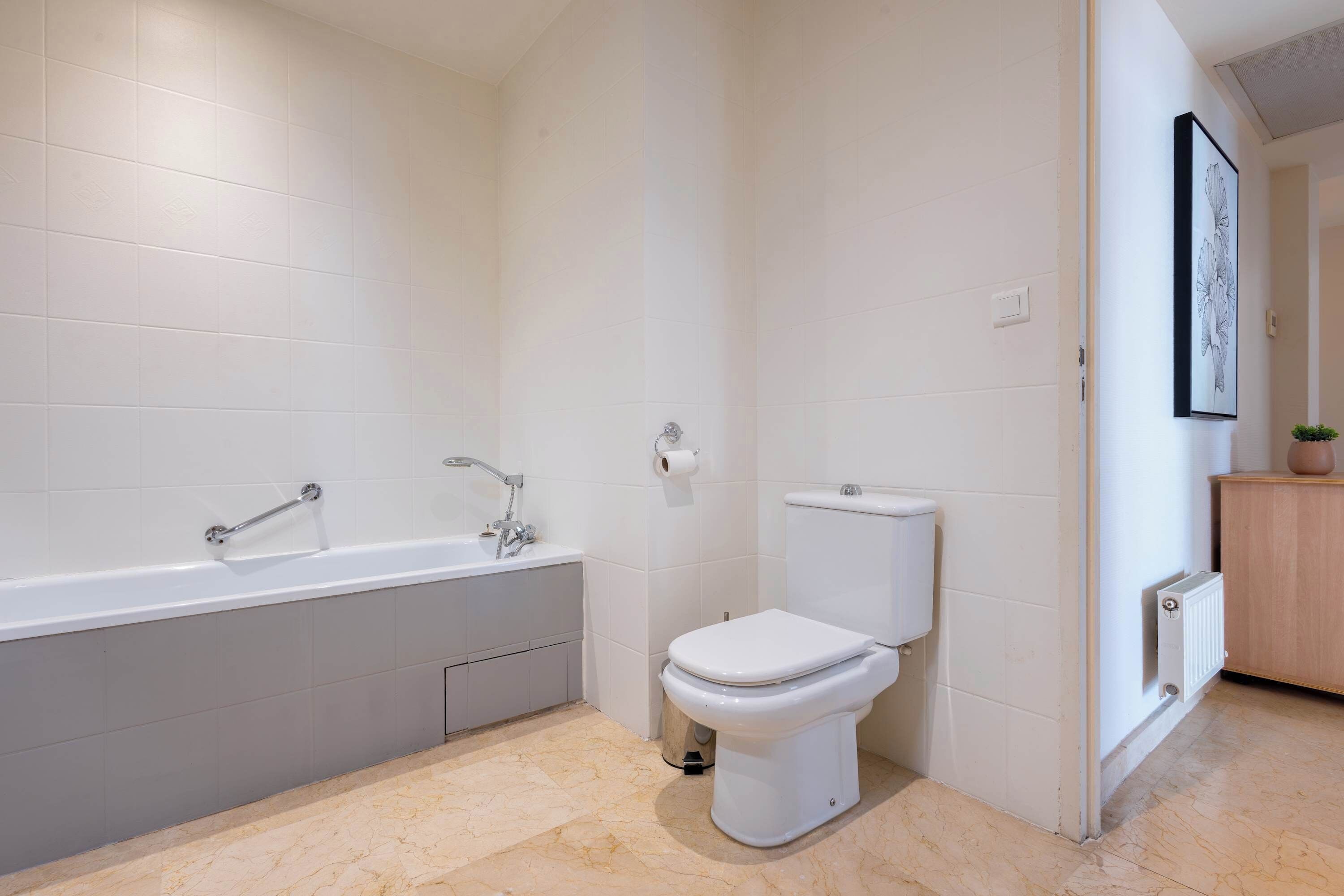 A modern bathroom with a bathtub, toilet, and a radiator.