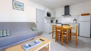 Un espacio habitable compacto con sofá, una mesa de comedor con sillas, y una cocina equipada con microondas, estufa y refrigerador.