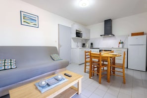 A compact living space with a sofa, a dining table with chairs, a kitchen area with a microwave, stove, and refrigerator.