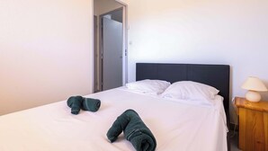 Habitación de hotel con una cama, almohadas, una mesita de noche de madera con una lámpara, y una puerta que da a otra habitación.