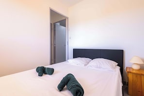 Une chambre d’hôtel avec un lit, des oreillers, une table de chevet en bois avec une lampe et une porte donnant sur une autre pièce.