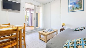 Una habitación con cama, televisión, mesa de comedor con sillas y vistas a través de un ventanal.