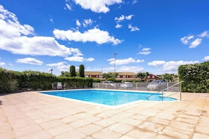 A swimming pool with a metal fence, a clear blue sky, and a residential building in the background.