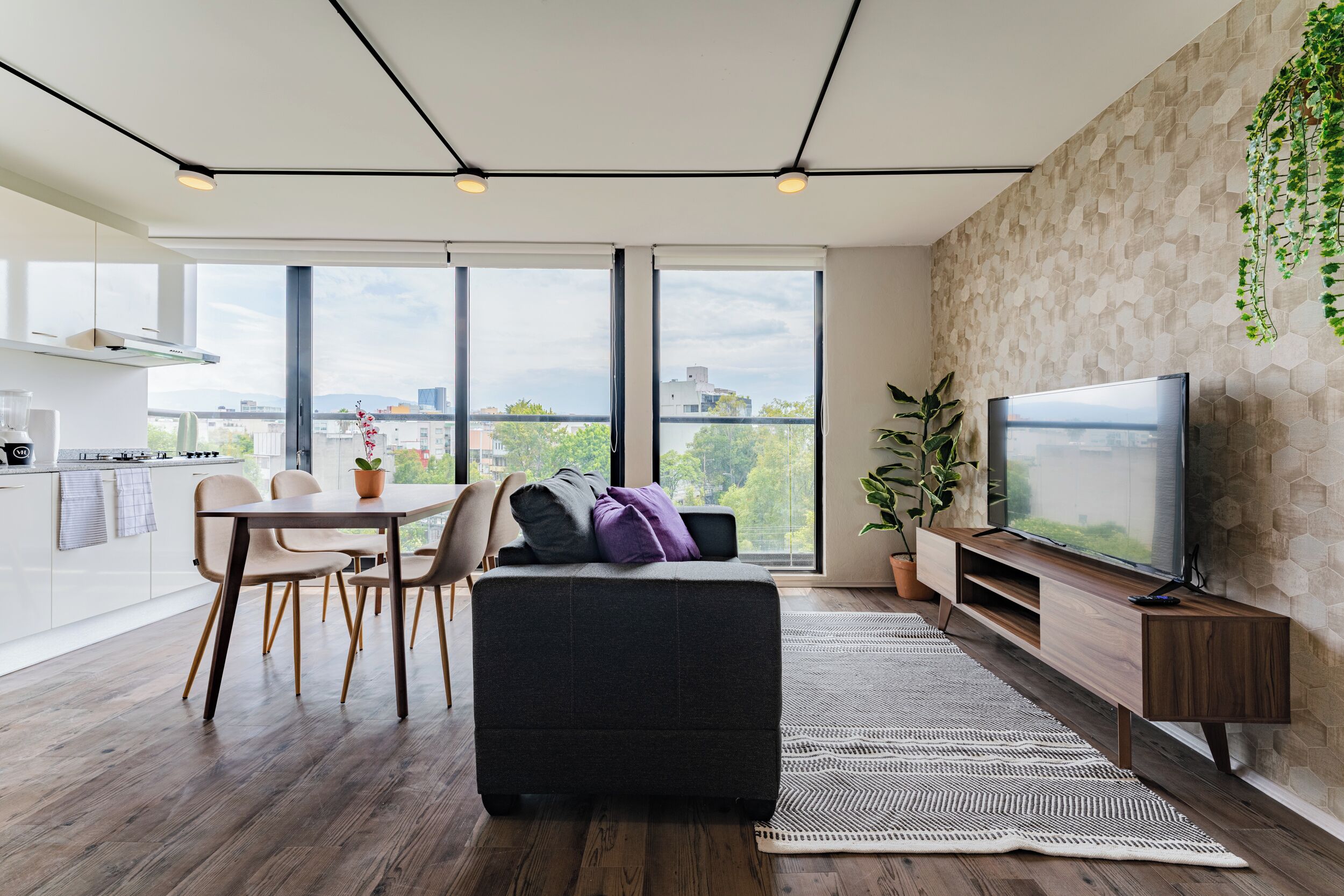 Een moderne woonkamer met een grote televisie, een eethoek met stoelen, een bank en een keuken op de achtergrond.