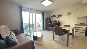 A modern living room with a sofa, a coffee table, and a dining area with a TV and kitchen counter. - Villa Bianca – Magnificent apartment with air conditioning (Sérignan)
