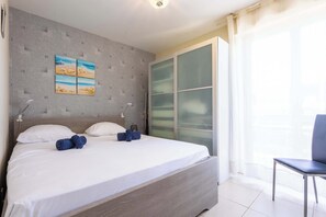 A neatly made bed with pillows and towels, a wall with a textured pattern and a painting, a sliding glass door, and a chair.