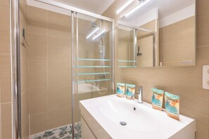 A bathroom with a glass-enclosed shower, a white sink, and a mirror.