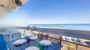 Ein Balkon mit Esstisch, der auf einen Strand und einen Parkplatz blickt.