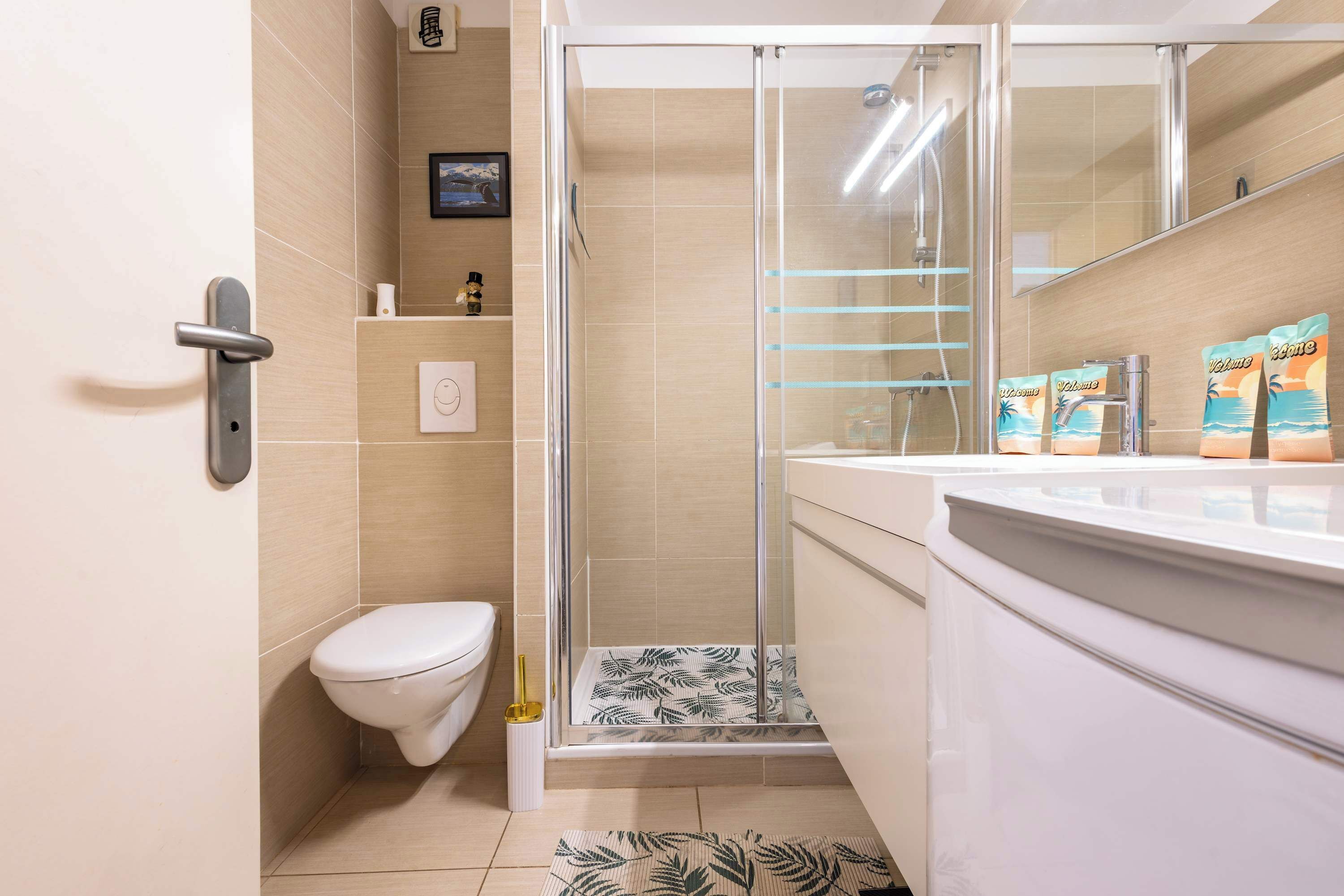 Un baño con inodoro, ducha con puerta de vidrio, lavamanos con artículos de aseo y espejo.