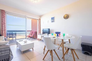 A modern living room with a dining area, a television, and a view of the beach.