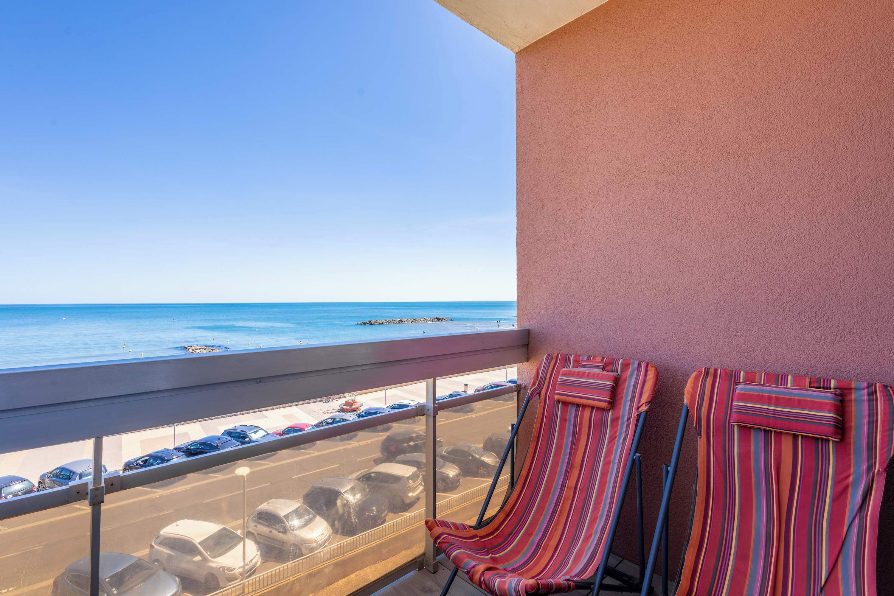 A balcony with a view of the beach and parked cars.