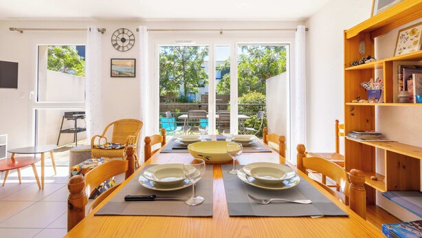 A dining area with a table set for two, a bookshelf, and a view of the outdoors. - Villa Bianca - Air-conditioned pavilion 500m from (Sérignan)