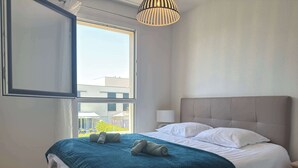 A hotel room with a large bed, a window, a bedside table with a lamp, and a ceiling light fixture.