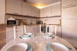 A modern kitchen with a microwave, coffee maker, and dining table set for four. - Cosy Cottage 150 m from the Beach (Valras-Plage)