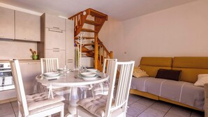 A dining area with a round table, white chairs, a wooden staircase, and a sofa.