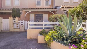 A residential building with a white fence, a covered patio, and a garden with plants and flowers.
