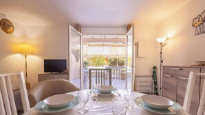 A dining table set with plates, glasses, and cutlery, a television, and a lamp in a room with a view to an outdoor area.