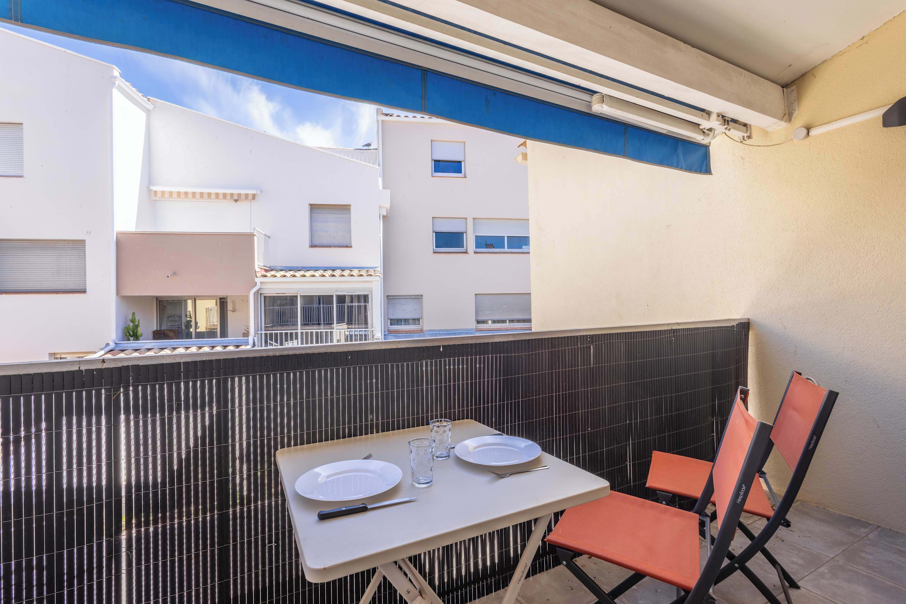 Un balcon avec une table dressée pour deux personnes, deux chaises et une vue sur les immeubles voisins.