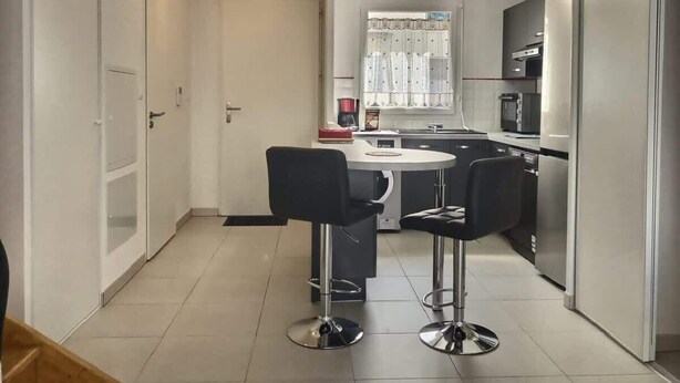 Une cuisine moderne dotée d’un îlot central, de deux tabourets de bar et d’appareils électroménagers en acier inoxydable.